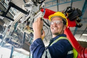 Male technician programs a robot arm with a digital tablet and assembly robot in a factory. Apprentice engineers programming robots in factory.